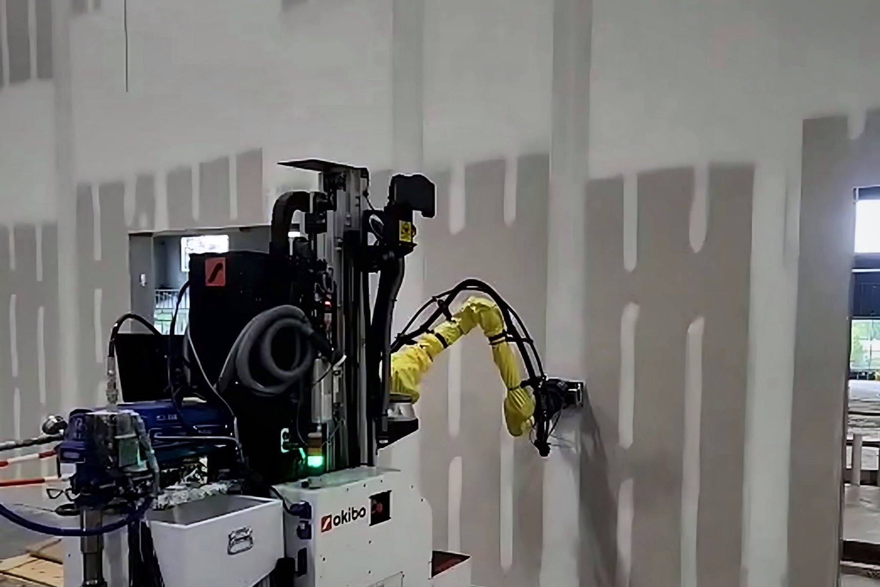Okibo EG7+ applying joint compound with a mud box on a taped warehouse wall