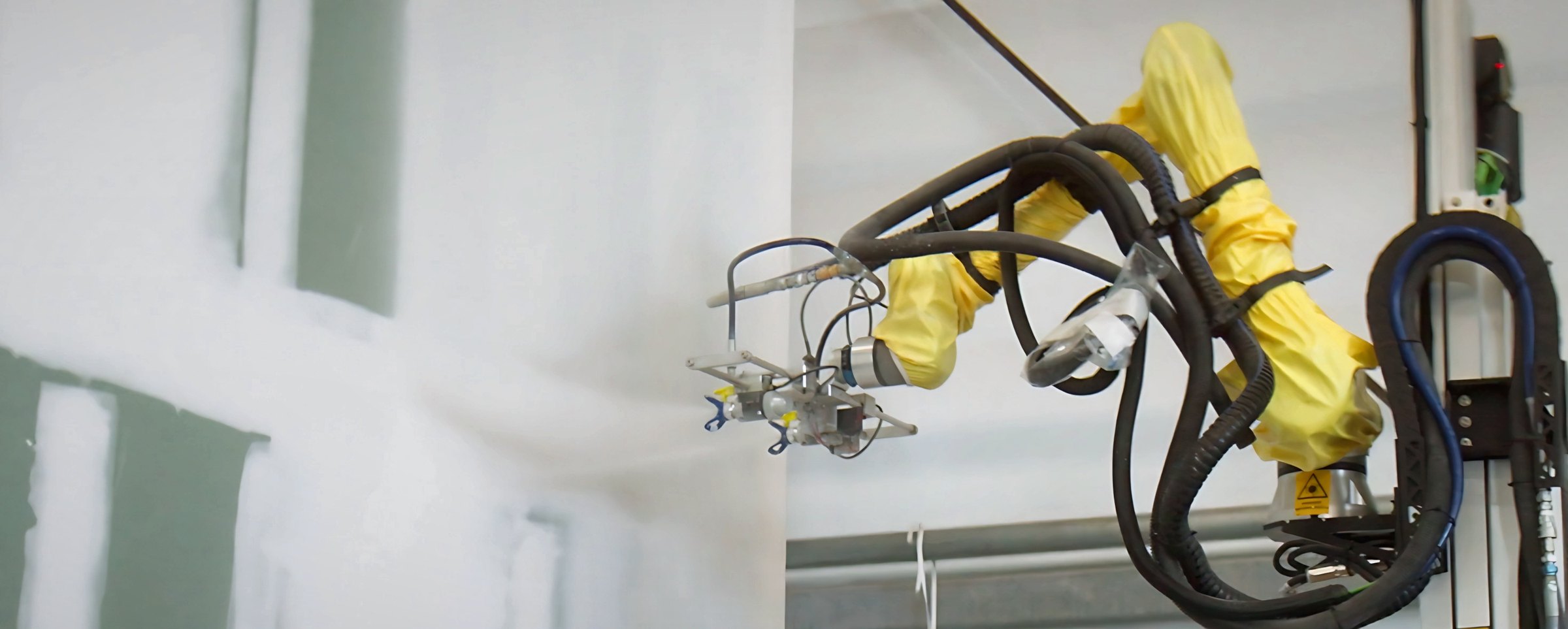 BLASTER™ dual-gun head spraying primer on a drywall wall